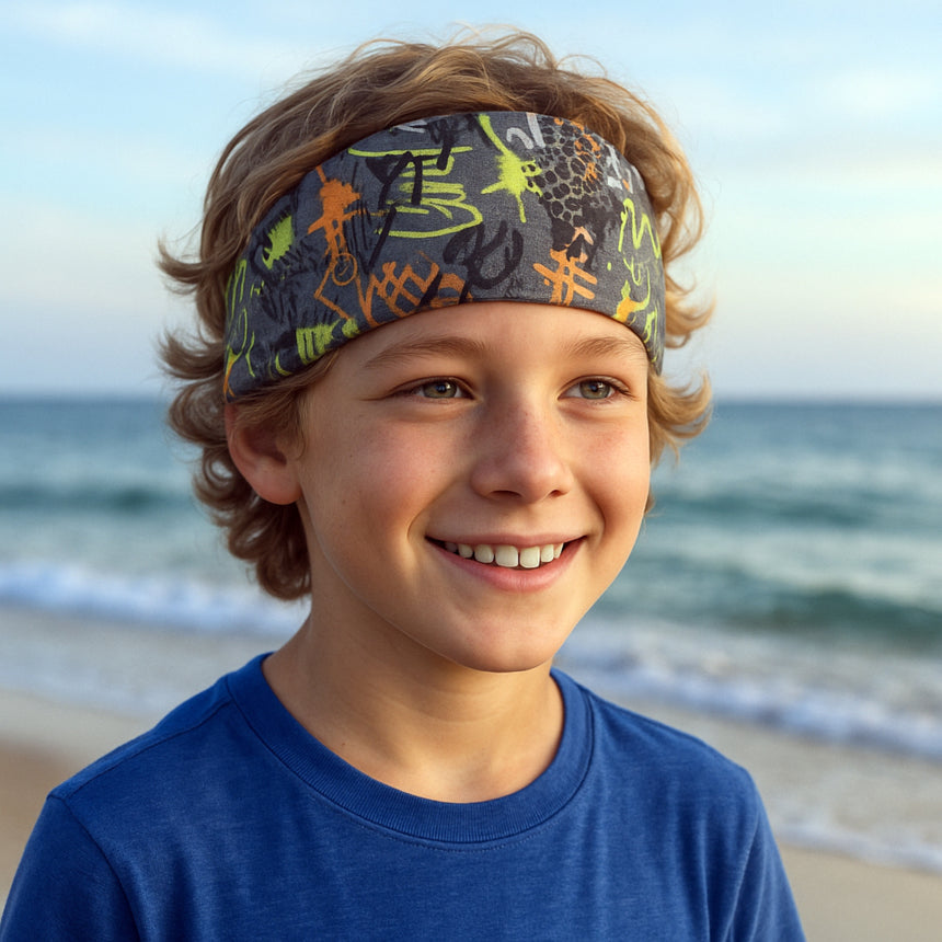 Junge am Strand trägt Wollhuhn Elastisches Öko Stirnband, handgemacht und zweilagig, ideal für Outdoor-Aktivitäten und unter Helmen tragbar. Perfekt für aktive Kinder.