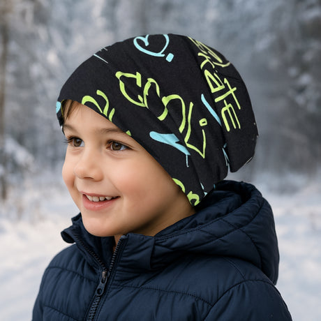 Kind mit Wollhuhn Öko Long Beanie lächelnd im Schnee, trägt eine zweilagige, weiche Beanie aus Baumwolljersey, ideal für ganzjährigen Komfort.