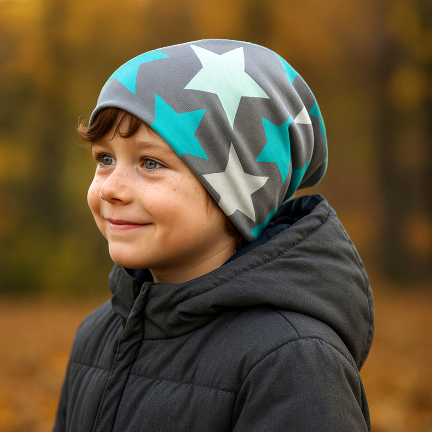 Kind mit Wollhuhn Öko Long Beanie, Wendemütze Big Stars Grau/Mint, lächelt im Wald. Perfekt für Herbst, aus weichem, dehnbarem Baumwolljersey, für ganzjähriges Tragen geeignet.