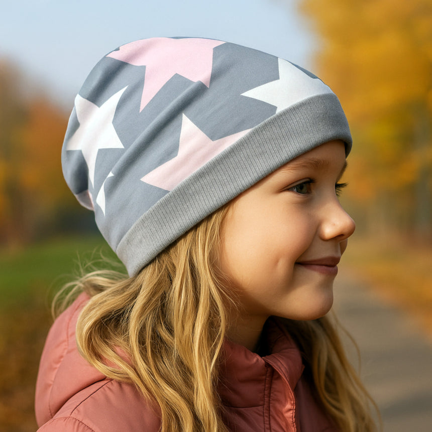 Ein Mädchen trägt die Wollhuhn Dünne Öko Beanie-Mütze mit großen Sternen, ideal für Übergangszeiten. Die Mütze ist handgemacht, bequem und dehnbar.