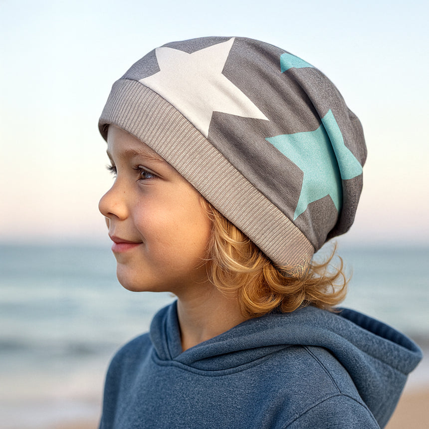 Kind am Wasser, trägt Wollhuhn Dünne Öko Beanie-Mütze Sommer/Übergang Einlagig Big Stars Sterne Grau/Mint. Handgemacht, dehnbar, ideal für Übergangszeiten.