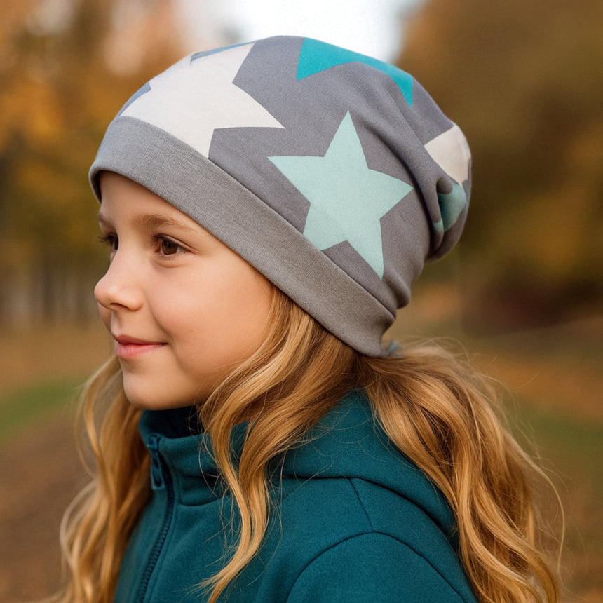 Mädchen trägt Wollhuhn Dünne Öko Beanie-Mütze Sommer/Übergang Einlagig Big Stars Sterne Grau/Mint, ideal für Herbst, mit elastischem Bündchen für angenehmen Tragekomfort.