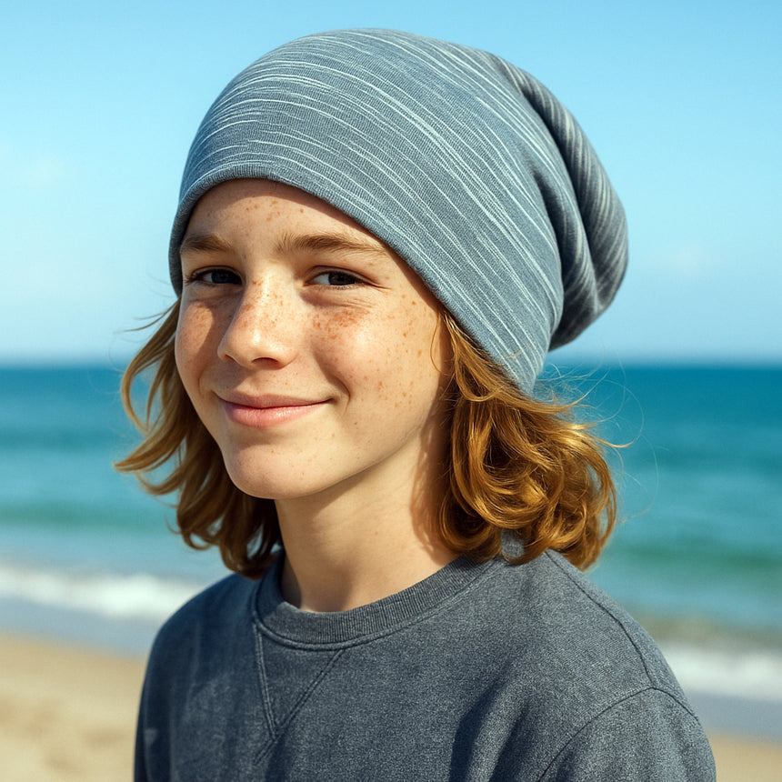 Junge mit grauer Wollhuhn Öko Long Beanie, zweilagig, lächelnd in die Kamera. Perfekte Passform für Komfort und Wärme, ideal für Kinder.