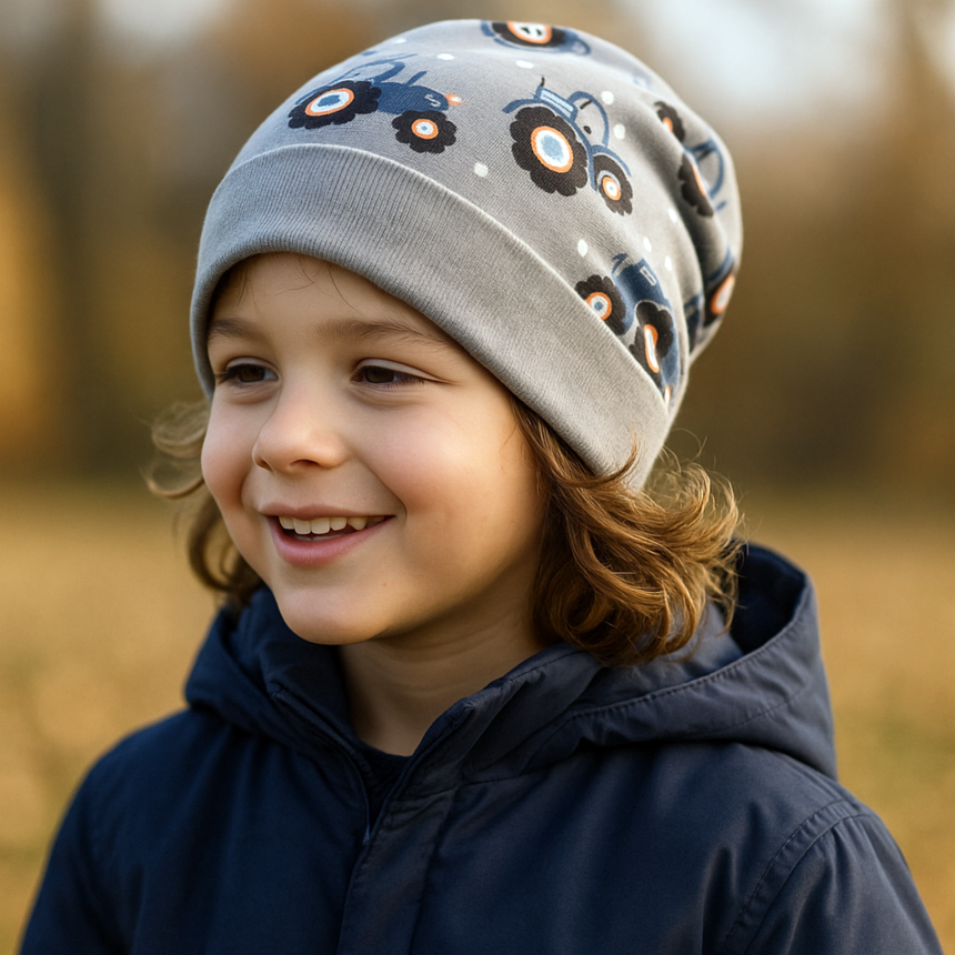 Kind im Herbstpark, trägt Wollhuhn Dünne Öko Beanie-Mütze, grau mit Traktormuster. Handgemacht, weich, ideal für Übergangswetter. Perfekt für aktive Kinder.
