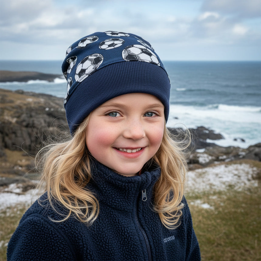 Kind mit blauen Augen trägt Wollhuhn Dünne Öko Beanie-Mütze Sommer/Übergang Einlagig Fußball Dunkelblau am windigen Strand.