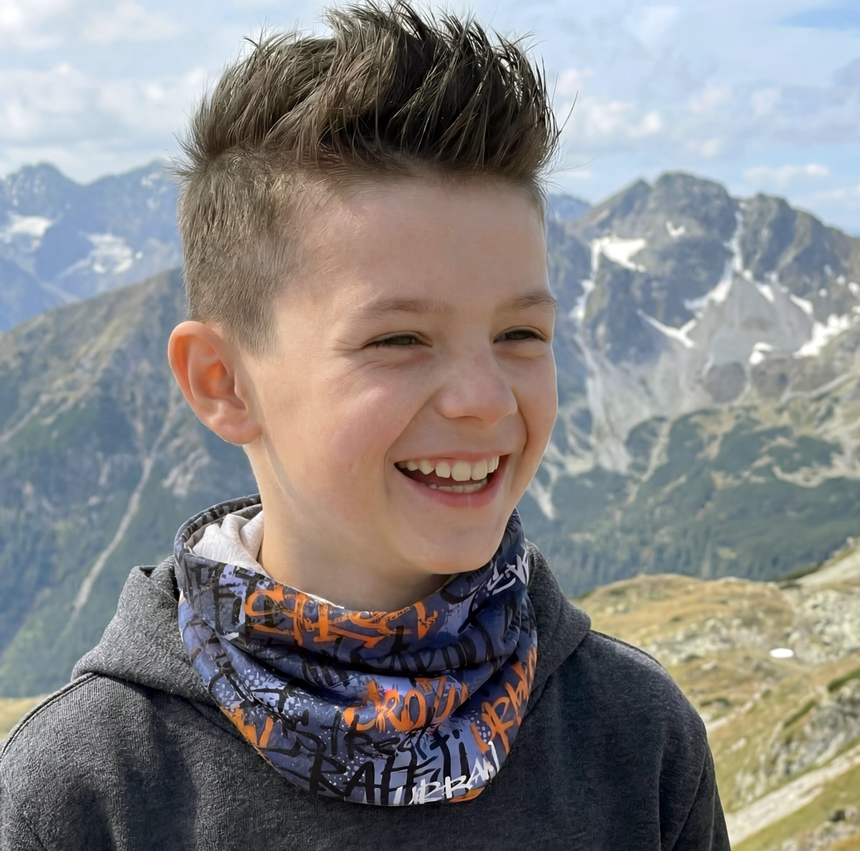 Junger Junge trägt Wollhuhn Leichtes Lockeres Öko Jersey Halstuch mit Graffiti-Muster in bergiger Landschaft; ideal für Übergangszeiten, handgefertigt in Deutschland.