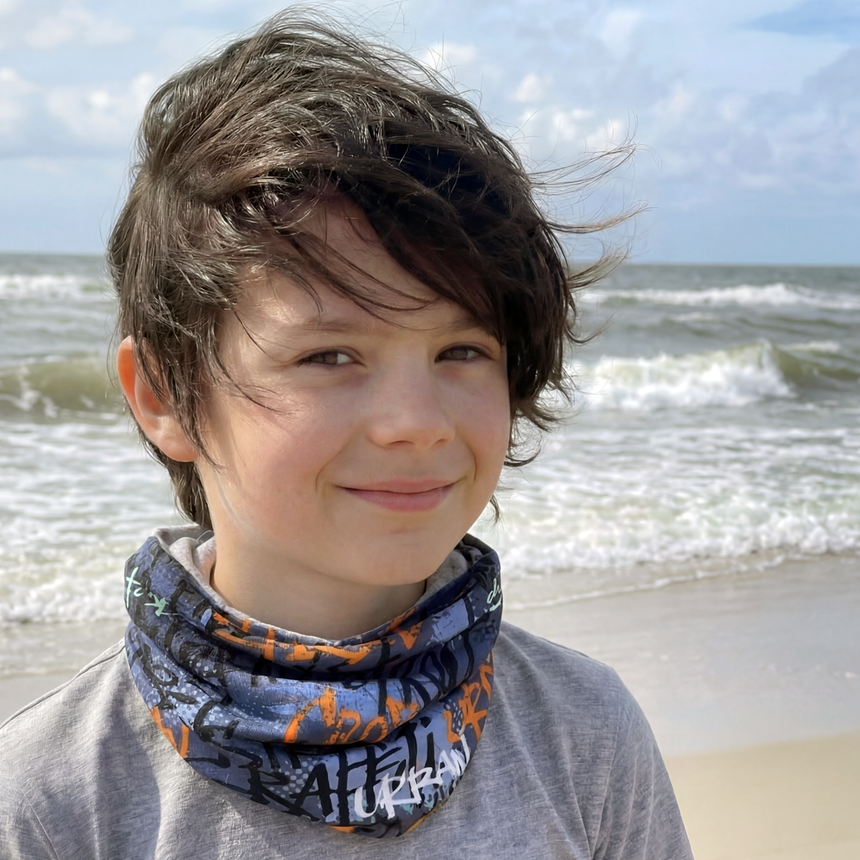 Junge am Strand trägt das Wollhuhn Leichtes Lockeres Öko Jersey Halstuch, ideal für Übergangszeiten; schützt vor Wind und Sonne, handgemacht in Deutschland.