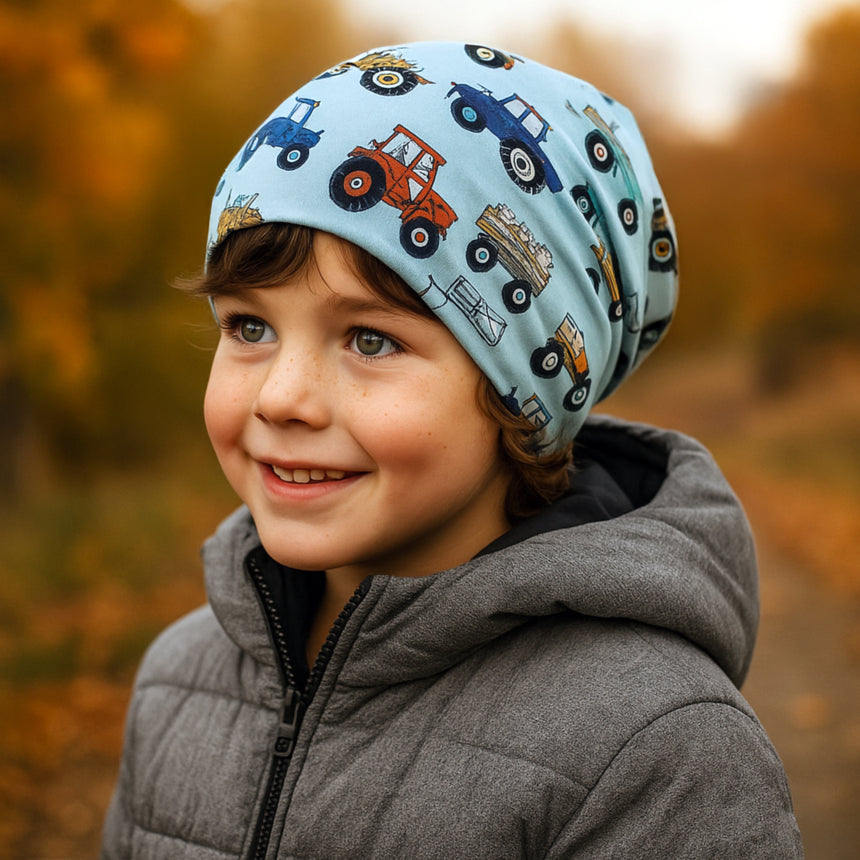 Kind trägt Wollhuhn Öko Long Beanie, zweilagig mit Traktor-Muster, ideal für Herbst/Winter. Bequem, dehnbar, aus weichem Öko-Jersey, perfekt für empfindliche Kinderhaut.