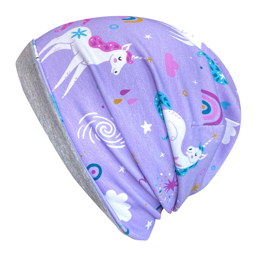 Wollhuhn Öko Long Beanie, zweilagig, mit Einhorn- und Sternmuster auf fliederfarbenem Stoff, ideal für Kinder. Wendemütze mit grauem Jerseyfutter, super bequem und ganzjährig tragbar.