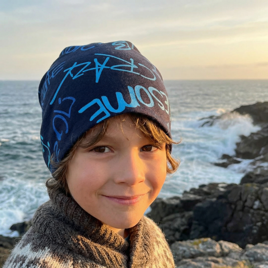 Kind mit Wollhuhn Öko Shorties Beanie am felsigen Ufer, warm gekleidet mit gestricktem Pullover. Ideal für aktive Kinder, handgemacht und doppellagig für zuverlässigen Schutz.