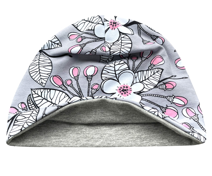 Wollhuhn Öko Shorties: Graue Beanie mit rosa-weißen Blumen, doppellagig und wendbar, handgenäht aus weichem Öko-Jersey für Komfort und Stil.