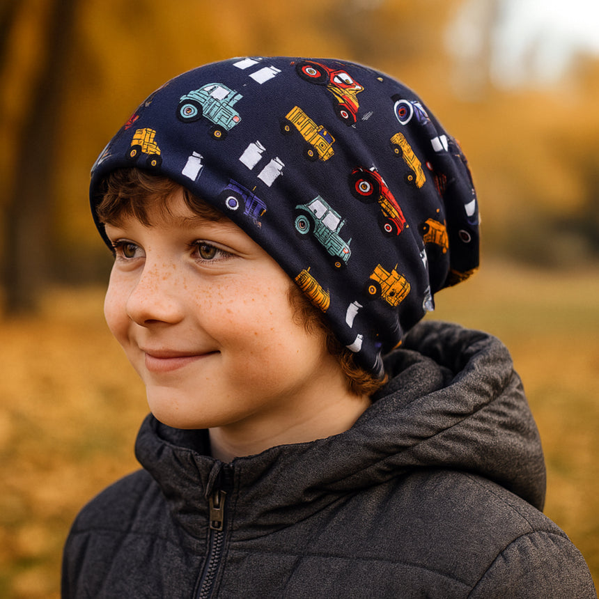 Junge mit Wollhuhn Öko Long Beanie, zweilagig, Traktor-Muster, lächelt im Herbst. Handgemacht in Deutschland für Komfort und Stil.