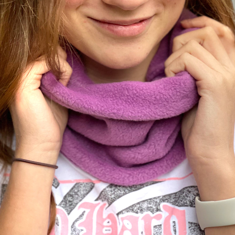 Frau trägt Wollhuhn WINTER Halstuch/Schlupfschal „Unser Wärmster“, doppellagiger Fleece in Flieder, handgemacht, einfach über den Kopf ziehen, ideal für kalte Tage.