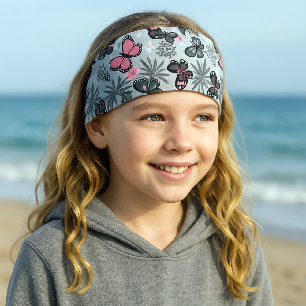 Mädchen am Strand trägt Wollhuhn Elastisches Öko Stirnband, zweilagig und breit, ideal für Outdoor-Aktivitäten. Handgemacht aus Bio-Baumwolle für Komfort und Vielseitigkeit.
