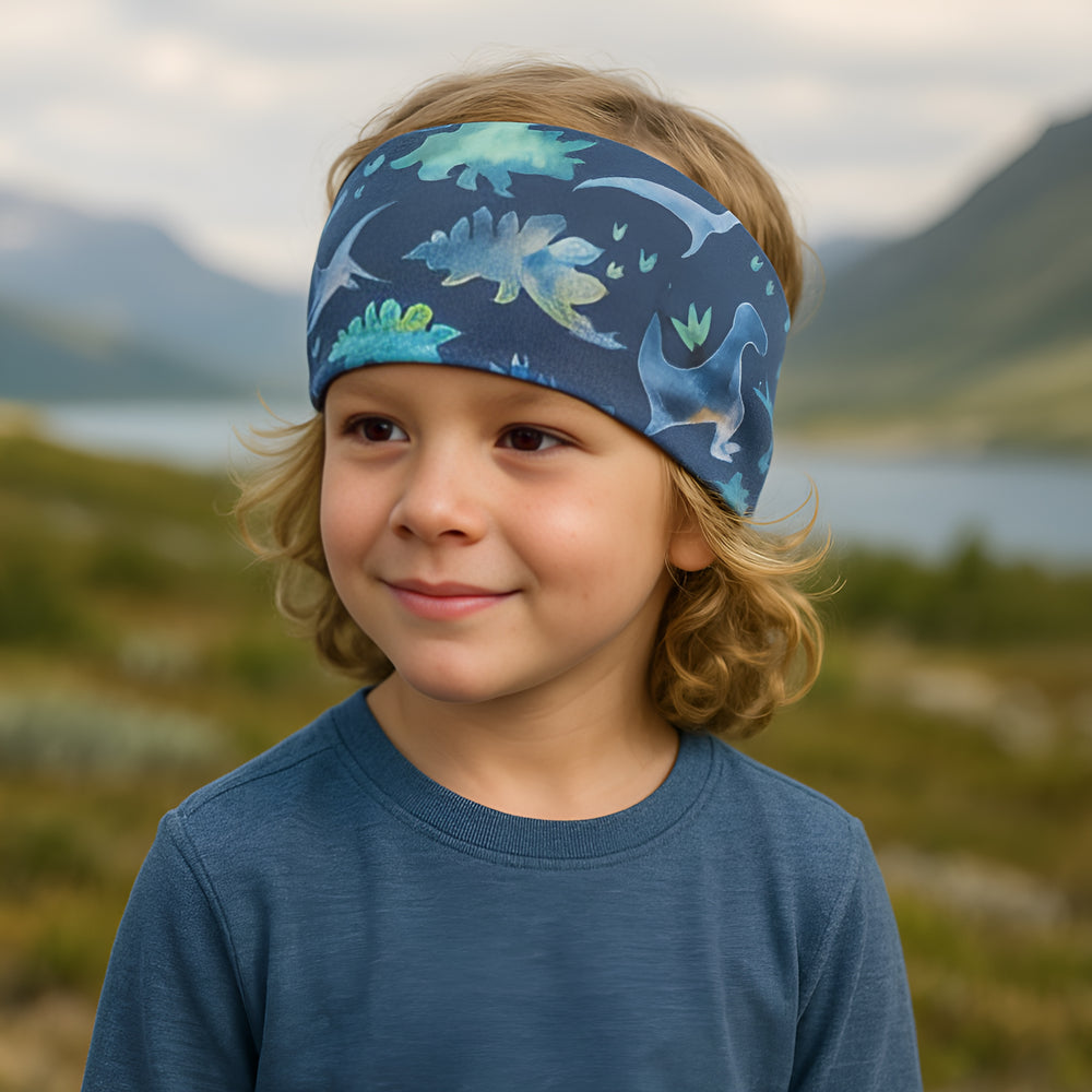 Kind trägt ein Wollhuhn Elastisches Öko Stirnband, zweilagig und breit, aus Jersey, in Blautönen mit Dinosaurier-Design. Ideal für Outdoor-Aktivitäten und handgefertigt.