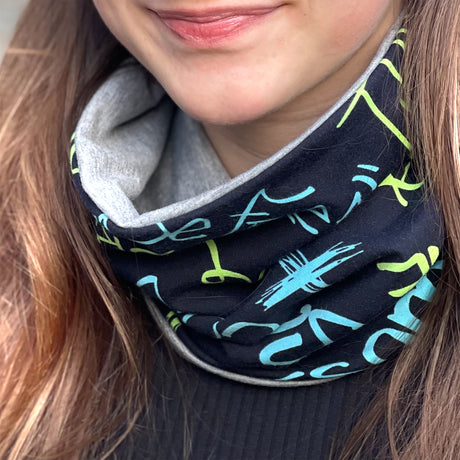 Frau trägt Wollhuhn LONG Loop, Jersey- oder Fleecefutter, Cool Music Schwarz; handgemachter, bequemer Schal, ideal für Schutz vor Wetter, passt Kindern und Erwachsenen.