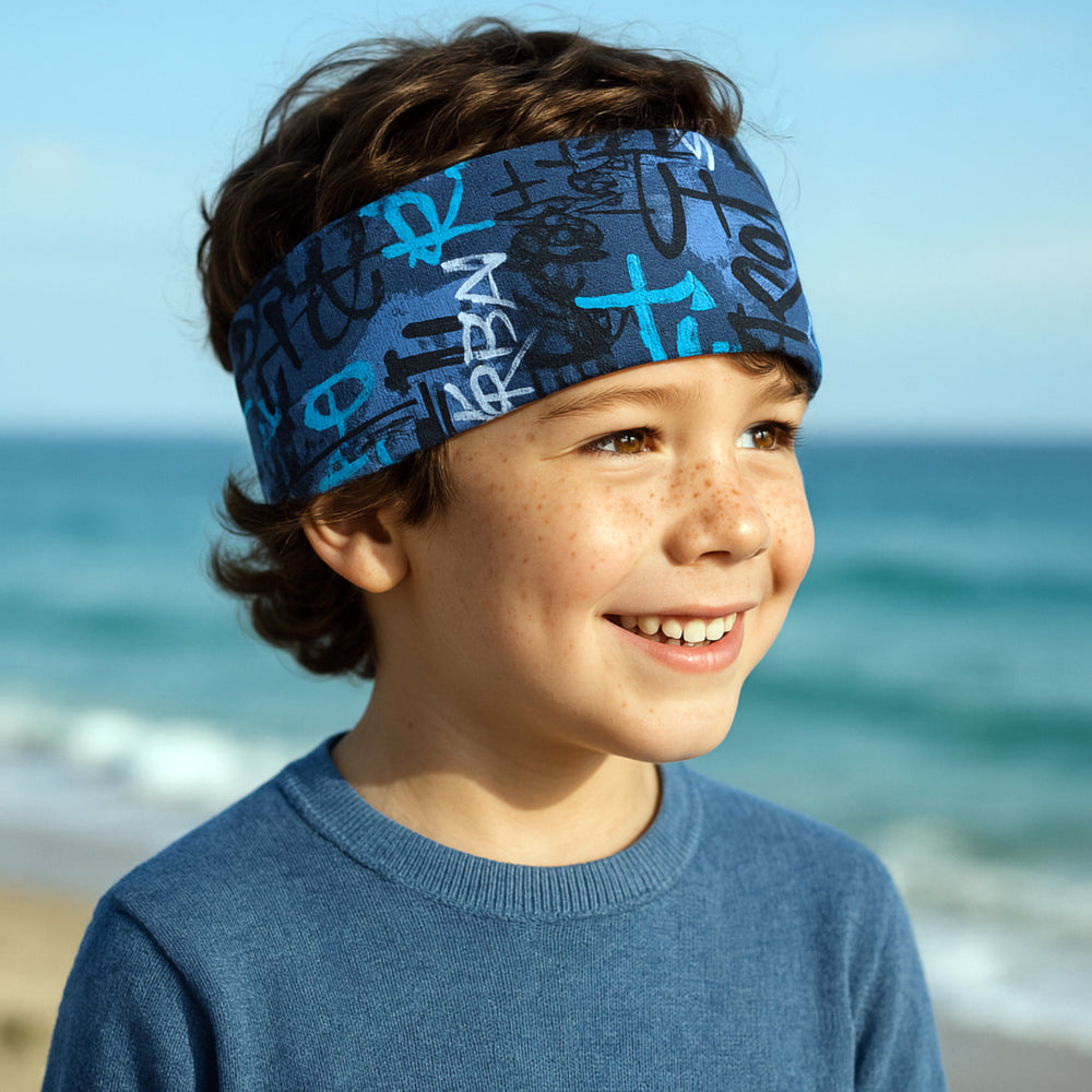 Junge am Strand trägt ein Wollhuhn Elastisches Öko Stirnband, zweilagig und breit, ideal für Outdoor-Aktivitäten, handgemacht aus Bio-Baumwolle.