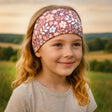 Mädchen trägt Wollhuhn Elastisches Öko Stirnband, zweilagig breit, mit Blumen/Blättern-Muster, ideal für Outdoor-Aktivitäten. Handgemacht aus Bio-Baumwolle, bequem und vielseitig.
