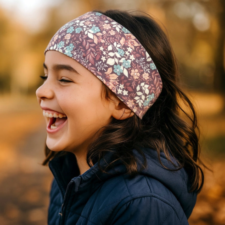 Mädchen mit blumenmusterigem Wollhuhn Stirnband aus Bio-Baumwolle, lacht im Herbst. Handgemacht, vielseitig und perfekt für Outdoor-Aktivitäten.