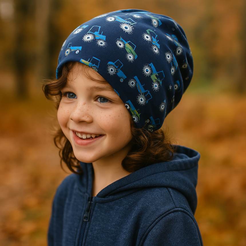 Ein Kind trägt die Wollhuhn Öko Long Beanie/Wendemütze mit Traktor-Motiven, ideal für kühle Tage, aus weichem, dehnbarem Baumwolljersey, handgefertigt in Deutschland.