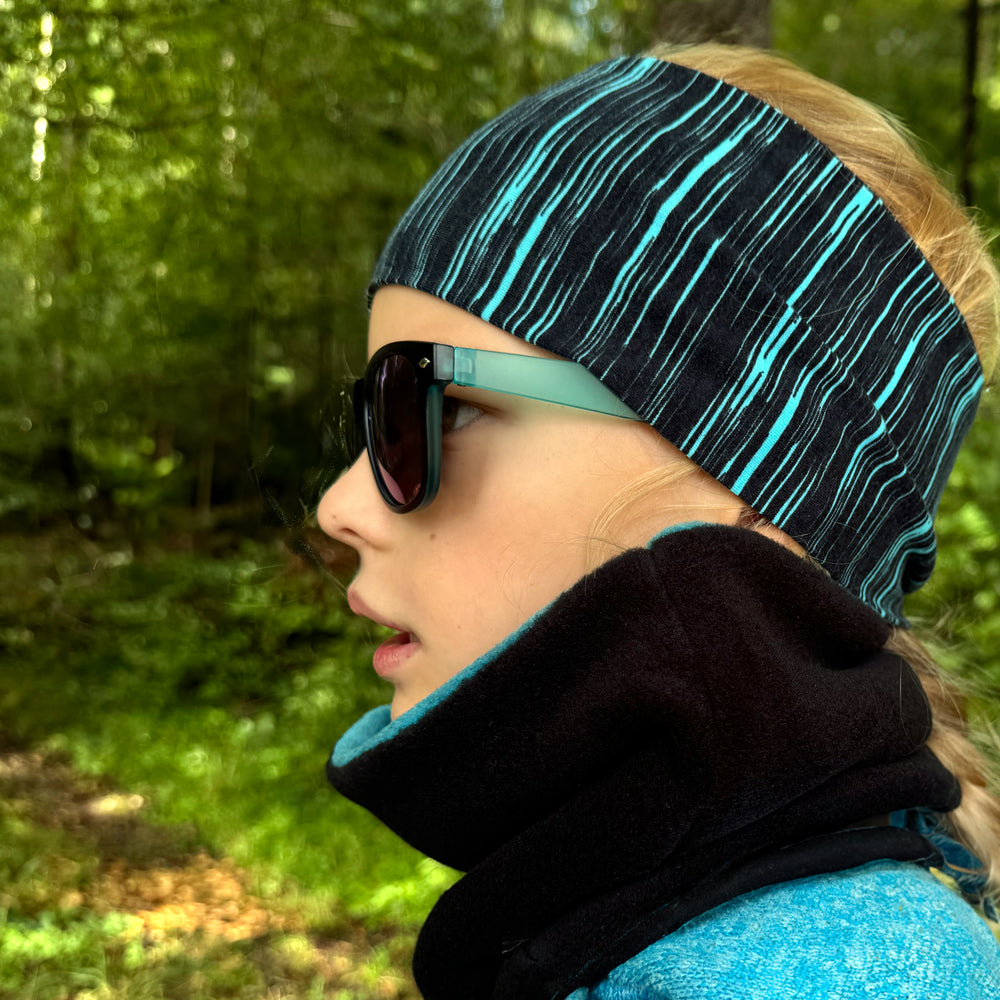 Mädchen trägt Wollhuhn Elastisches Öko Stirnband, Jersey zweilagig breit, ideal für Schule und Sport, handgemacht aus Bio-Baumwolle. Perfekt für Outdoor-Aktivitäten.