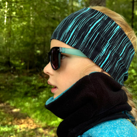 Mädchen trägt Wollhuhn Elastisches Öko Stirnband, Jersey zweilagig breit, ideal für Schule und Sport, handgemacht aus Bio-Baumwolle. Perfekt für Outdoor-Aktivitäten.