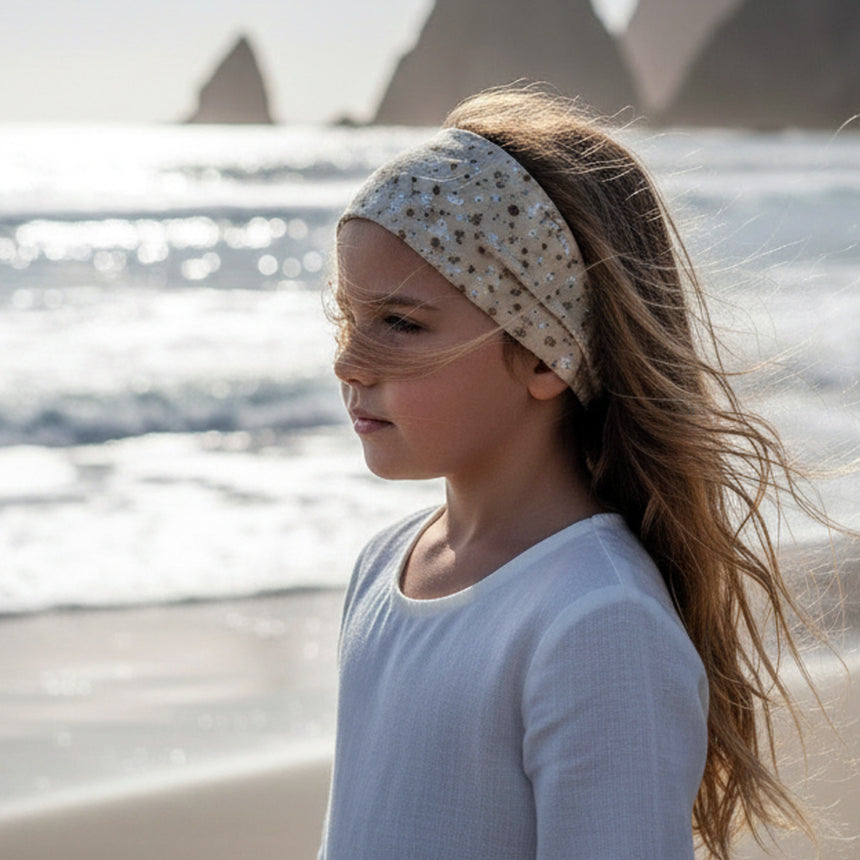 Mädchen am Strand mit Wollhuhn Elastisches Öko Stirnband, Jersey, zweilagig, breit. Wind weht ihr Haar, Blick aufs Meer, Stirnband aus Bio-Baumwolle.