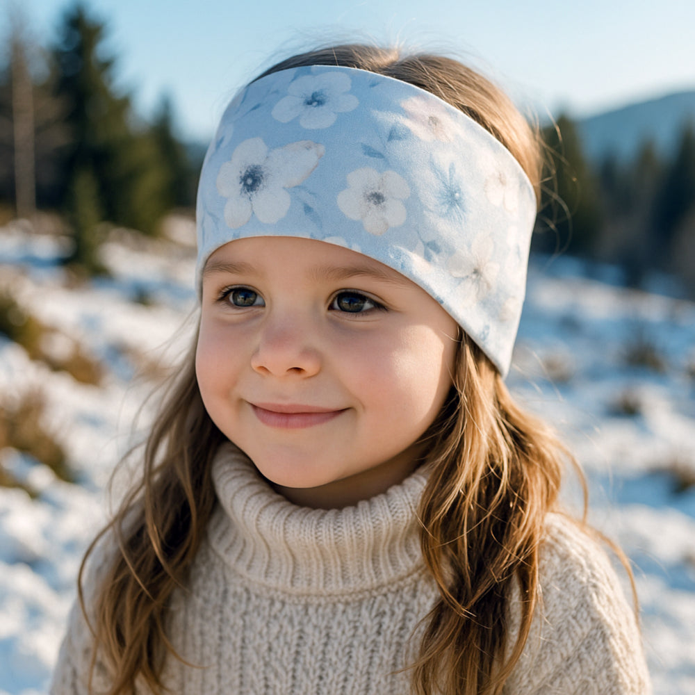 Mädchen trägt ein Wollhuhn Elastisches Öko Stirnband/Haarband Jersey Zweilagig Breit in der Schneelandschaft, lächelnd und mit einem handgemachten, bequemen Stirnband aus Bio-Baumwolle.