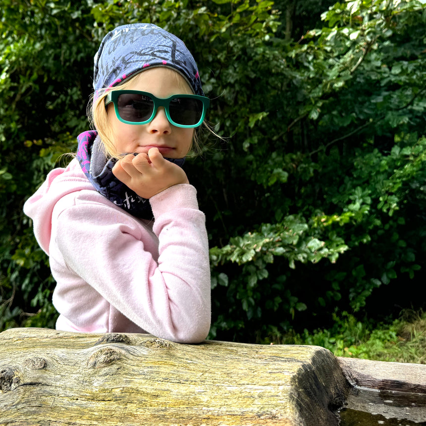 Mädchen mit Sonnenbrille trägt Wollhuhn Öko Long Beanie, Wendemütze, zweilagig, ideal für das ganze Jahr und bequem für Kinder.