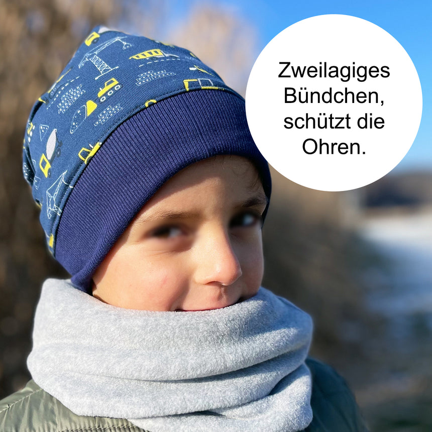 Kind trägt Wollhuhn Dünne Öko Beanie-Mütze Sommer/Übergang Einlagig Blockstreifen Blau/Grau, handgemacht, aus weichem Öko-Jersey, ideal für Übergangszeiten.