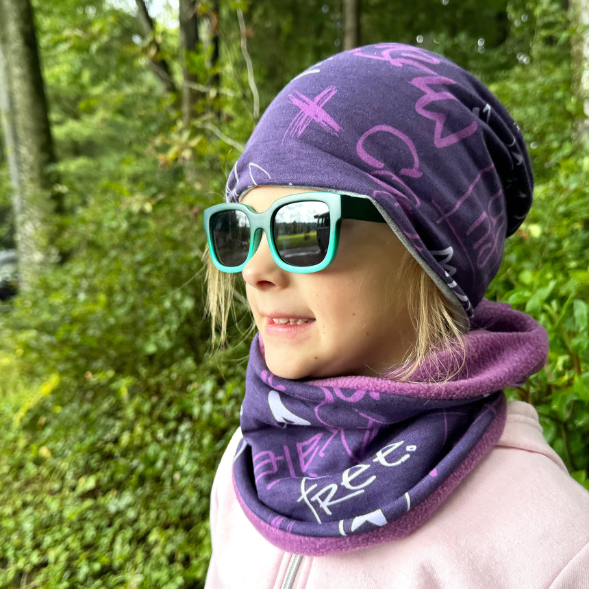Mädchen trägt Wollhuhn Öko Long Beanie Wendemütze, zweilagig, bequem und modisch. Perfekt für ganzjähriges Tragen, ideal für Kinder, violette Beanie.