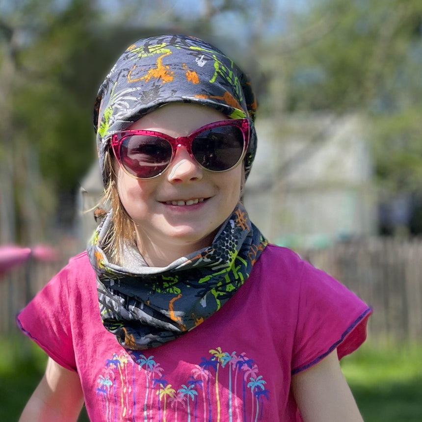 Mädchen trägt Wollhuhn Leichtes Öko Jersey Halstuch, perfekt für Übergangszeiten, mit Sonnenbrille und Schal als modisches Accessoire im Freien.