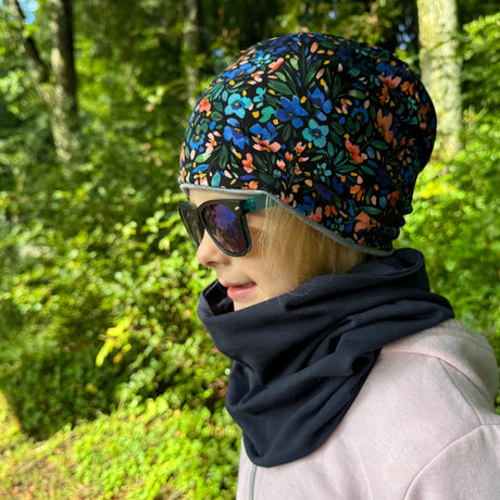 Mädchen trägt Wollhuhn Öko Long Beanie/Wendemütze: zweilagig, aus weichem Baumwolljersey, bequem, ideal für Kinder, handgemacht in Deutschland, mit floralem Muster.