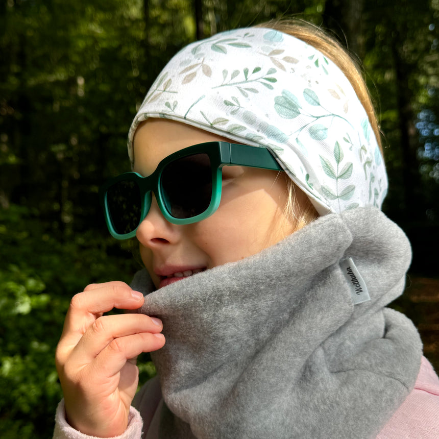 Mädchen mit Wollhuhn Elastisches Öko Stirnband Jersey Zweilagig, Aquarellblätter-Design, trägt Sonnenbrille und Schal. Ideal für Schule und Outdoor-Aktivitäten, handgemacht in Deutschland.