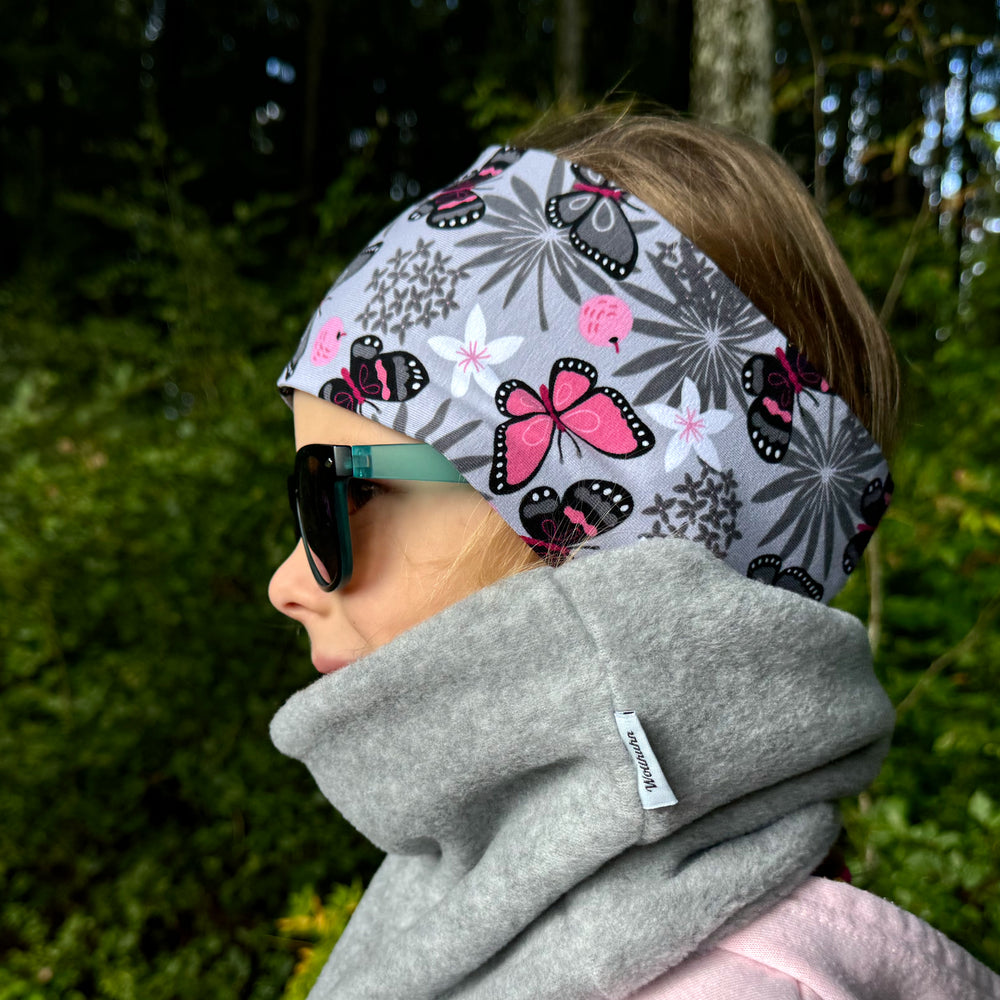 Frau trägt Wollhuhn Elastisches Öko Stirnband – zweilagig, breit, mit Schmetterlingsmotiv. Handgemacht aus Bio-Baumwolle, ideal für Outdoor-Aktivitäten.
