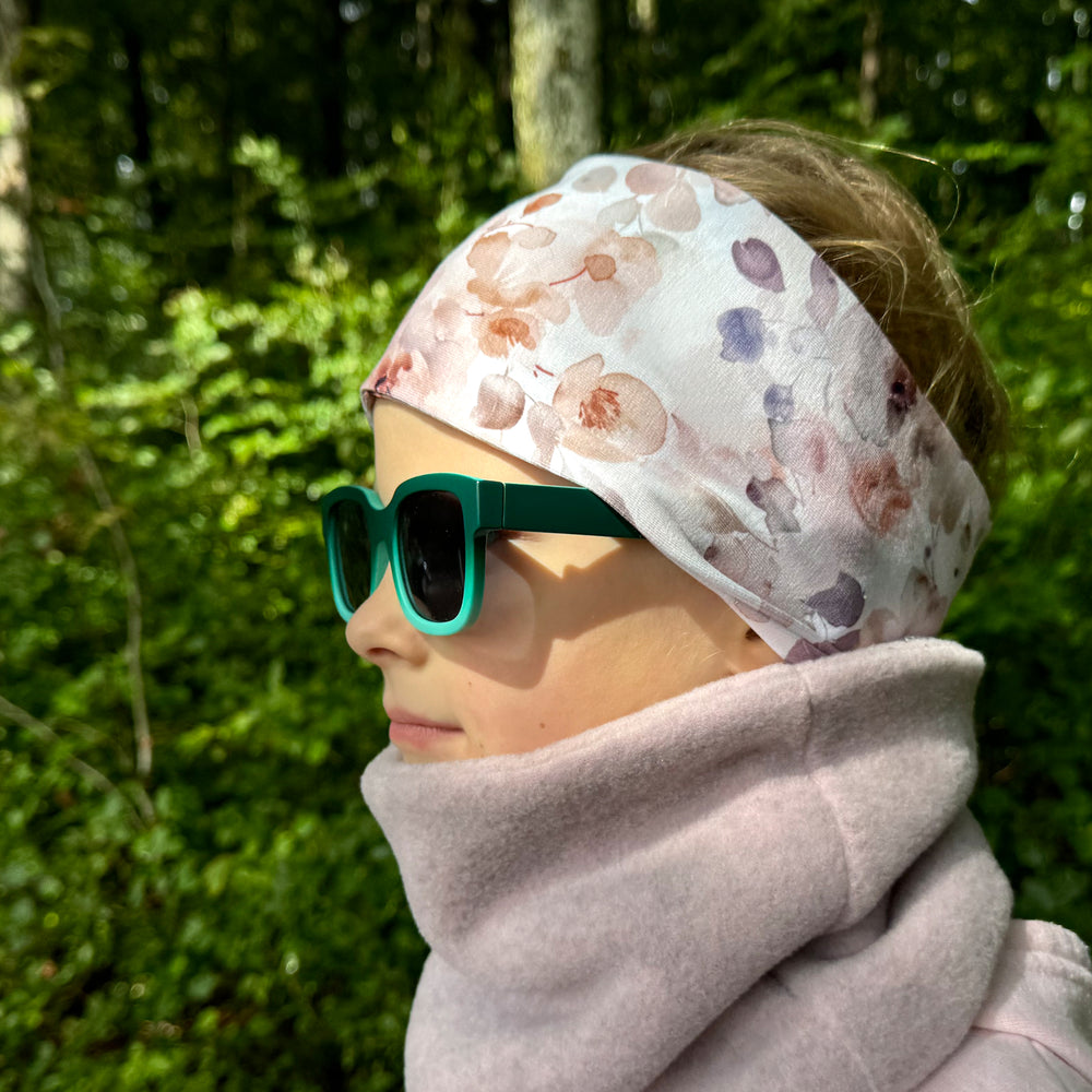 Frau trägt Wollhuhn Elastisches Öko Stirnband / Haarband Jersey Zweilagig Breit Aquarellblumen Altrosa, handgemacht, weich und vielseitig für Outdoor-Aktivitäten.