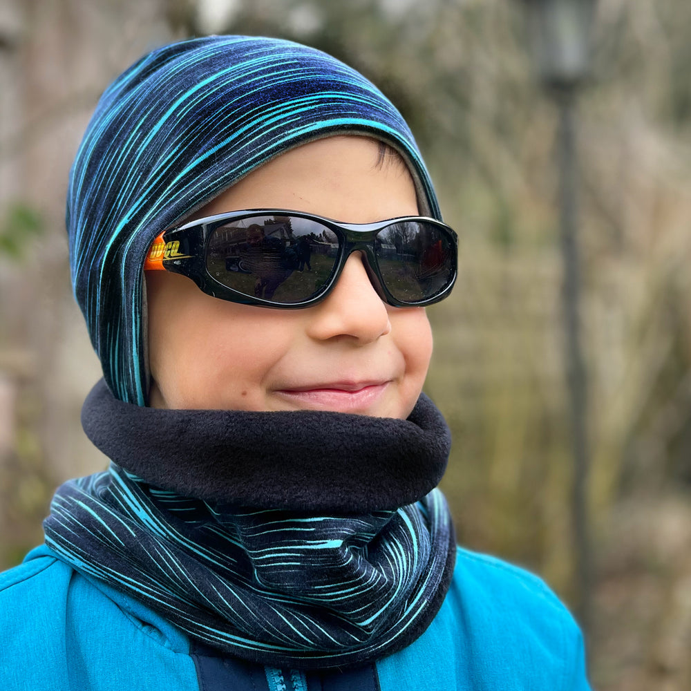 Junge mit Wollhuhn Öko Shorties, zweilagige Wendemütze, trägt Sonnenbrille und Schal, handgemacht aus Öko-Jersey für Komfort und stilvolles Aussehen.