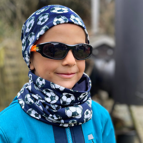 Junge trägt Wollhuhn Öko Long Beanie in Dunkelblau mit Fußball-Design und Sonnenbrille. Bequeme, zweilagige Wendemütze aus weichem Öko-Jersey, ideal für Kinder.