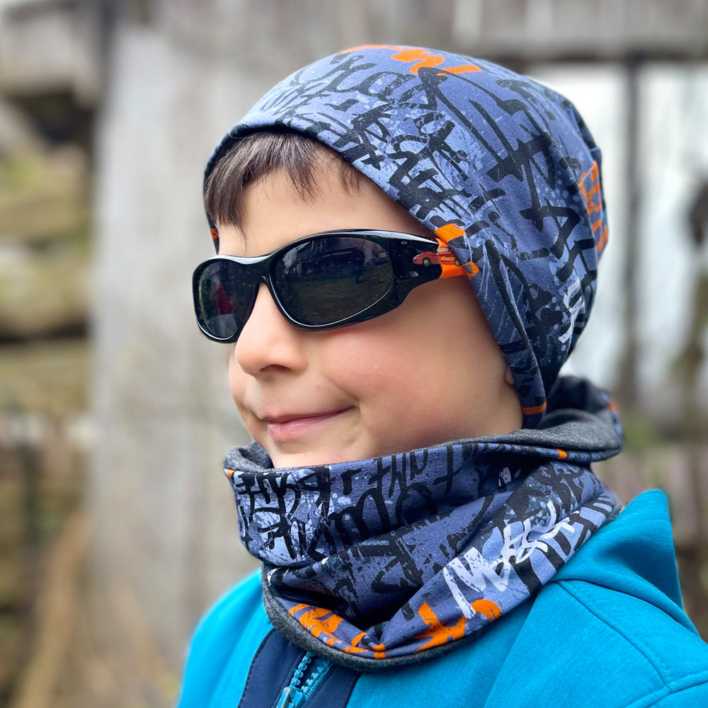 Junge trägt Wollhuhn Öko Shorties Wendemütze, stylisch und bequem, mit Sonnenbrille und Schal, ideal für aktive Kinder, handgefertigt in Deutschland.