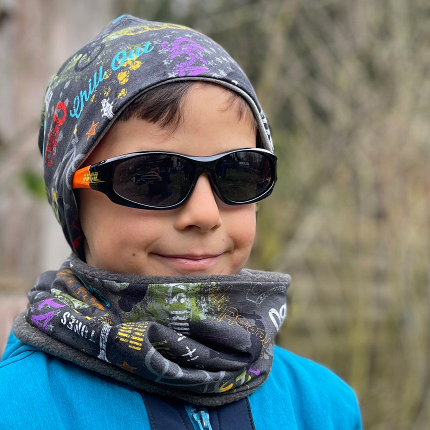 Junge mit Sonnenbrille und Schal trägt Wollhuhn Öko Shorties, eine zweilagige, handgemachte Wendemütze in Anthrazit, ideal für aktive Kinder.