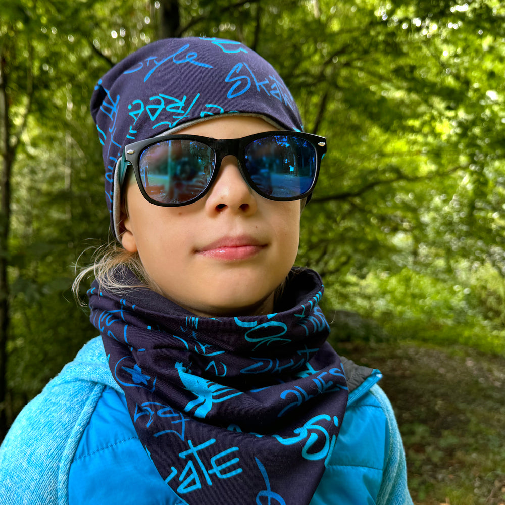 Mädchen mit Sonnenbrille und Wollhuhn Öko Shorties Beanie, handgemachte, zweilagige Mütze, ideal für aktive Kinder, stilvoll und bequem.
