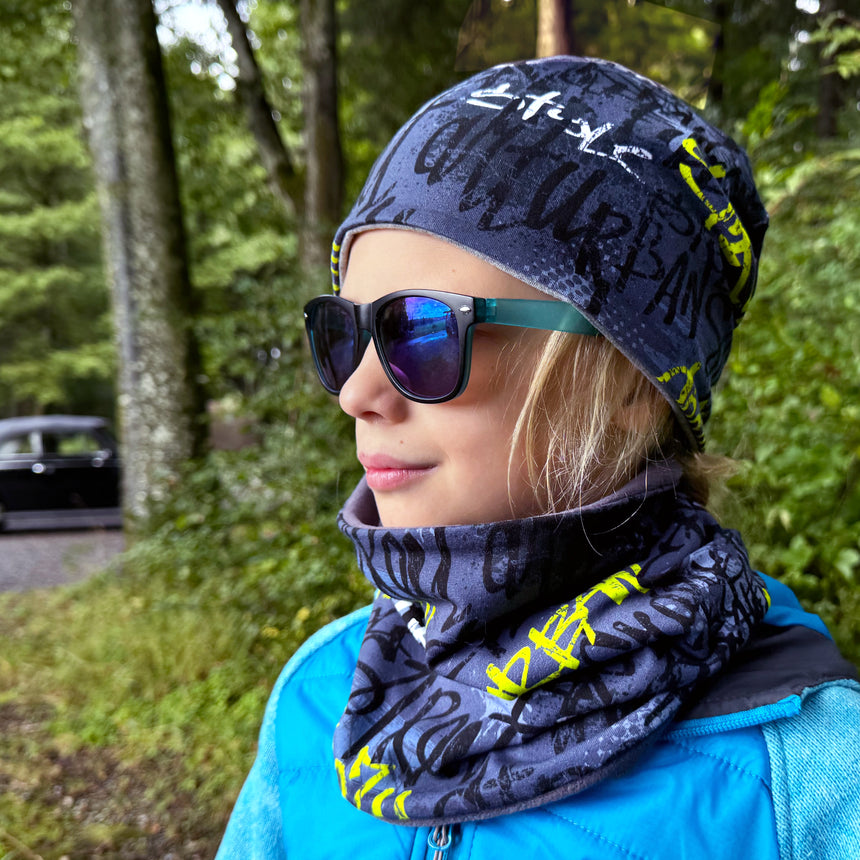 Mädchen trägt Wollhuhn Öko Shorties Wendemütze, zweilagig, ideal für aktive Kinder. Handgemacht, bequem, passt unter Helme, hält Ohren warm.