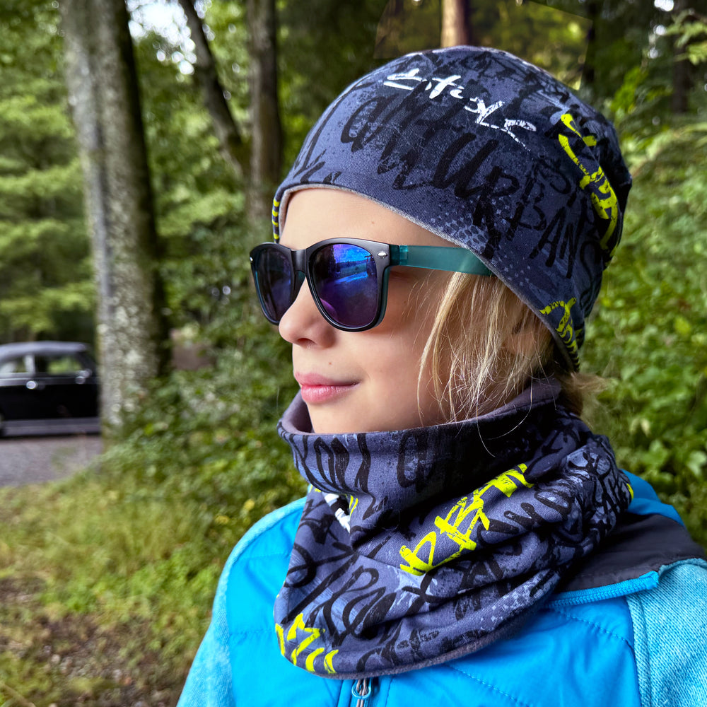 Mädchen trägt Sonnenbrille und Beanie, präsentiert den Wollhuhn LONG Loop Schal, der Komfort und Stil bietet, ideal für alle Altersgruppen.