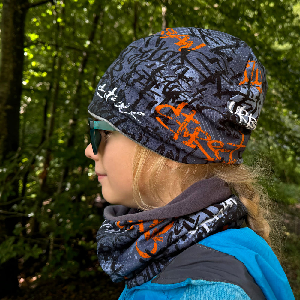 Frau im Wald mit Wollhuhn Öko Shorties Beanie, handgemacht, wendbar, ideal für aktive Kinder, bequem unter Helmen tragbar.
