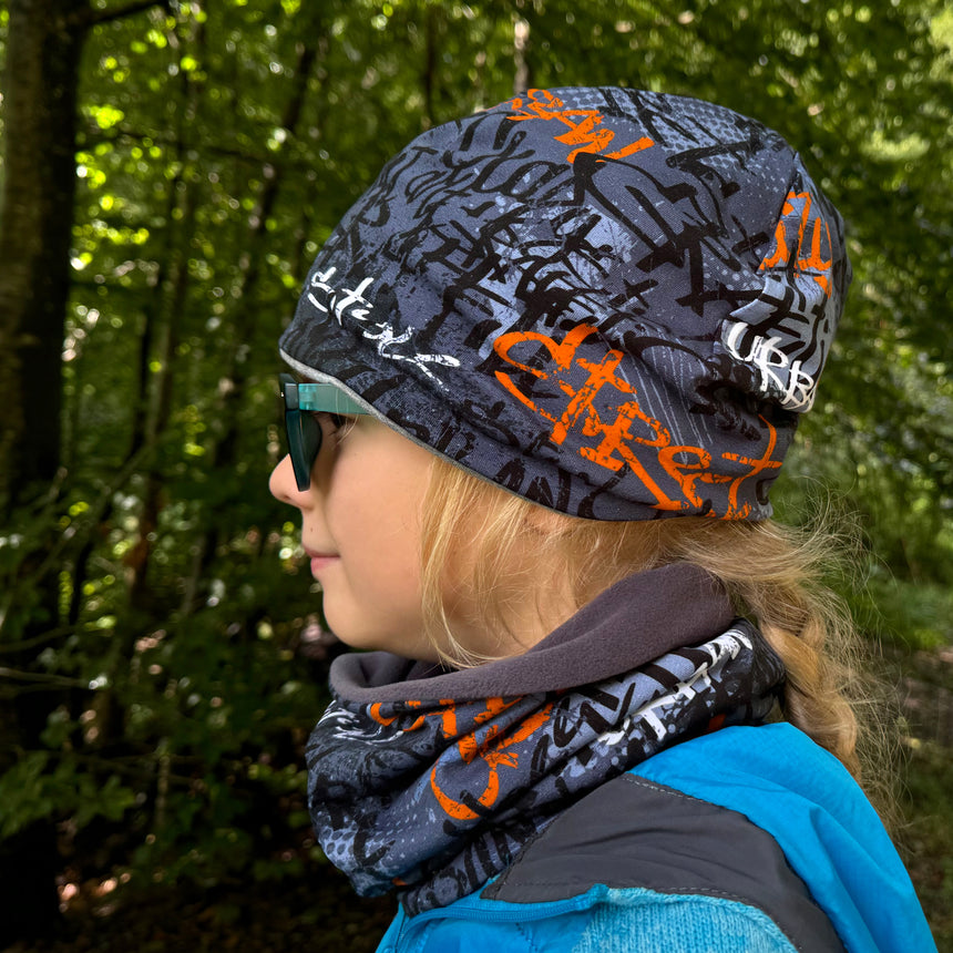 Frau im Wald mit Wollhuhn Öko Shorties Beanie, handgemacht, wendbar, ideal für aktive Kinder, bequem unter Helmen tragbar.