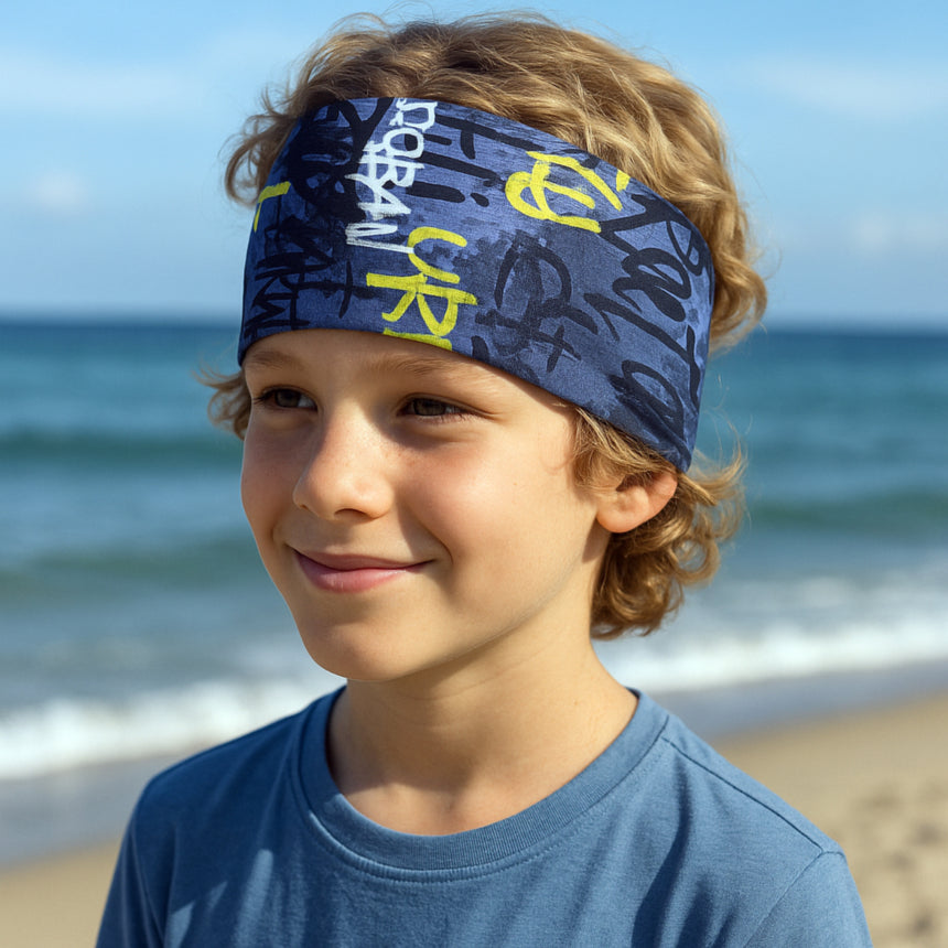 Junge trägt Wollhuhn Elastisches Öko Stirnband auf Strand, handgemacht und zweilagig für Komfort und Vielseitigkeit. Ideal für Sport und Outdoor-Aktivitäten.