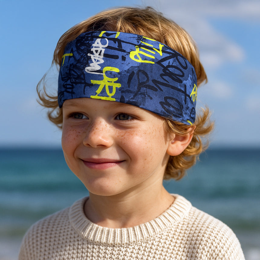 Junge am Strand trägt Wollhuhn Elastisches Öko Stirnband aus Jersey, handgemacht, vielseitig, ideal für Outdoor-Aktivitäten, schützt Ohren und passt unter Helme.