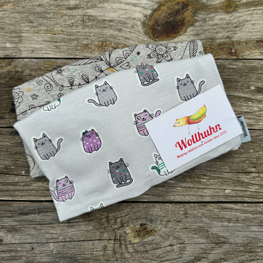 Beanie Überraschungstüte mit gefalteten Decken und Katzendruck auf Holzoberfläche, repräsentativ für Wollhuhns handgefertigte, hochwertige Mützenangebote.