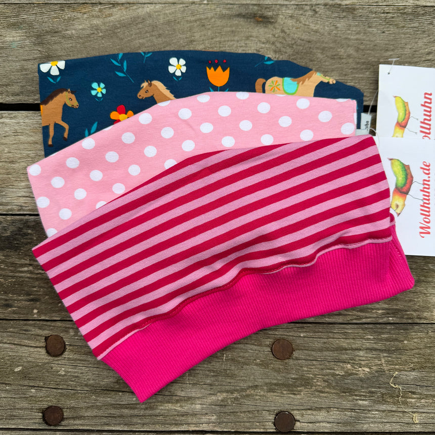 Beanie Überraschungstüte: Stapel von pink-blauen und gestreiften Mützen, handgefertigt in Deutschland, ideal für Adventskalender oder Geschenke. Hochwertige Qualität, nachhaltig produziert.
