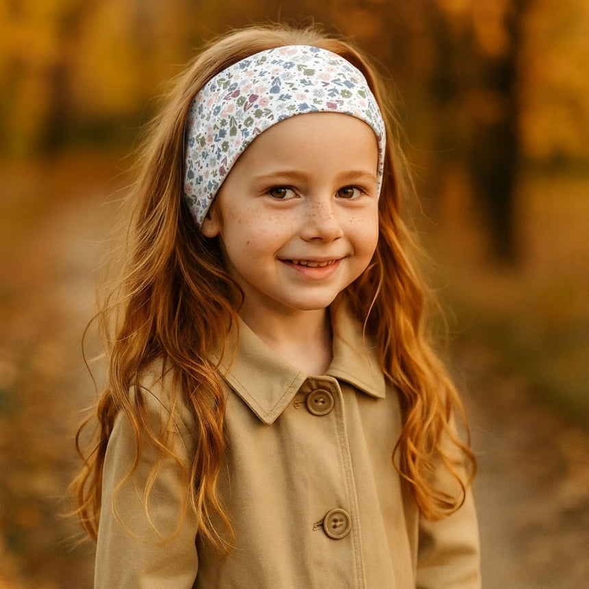 Mädchen mit Wollhuhn Elastisches Öko Stirnband, Jersey zweilagig, Blümchenmuster. Trägt camel-farbene Jacke, lächelt in herbstlicher Umgebung.